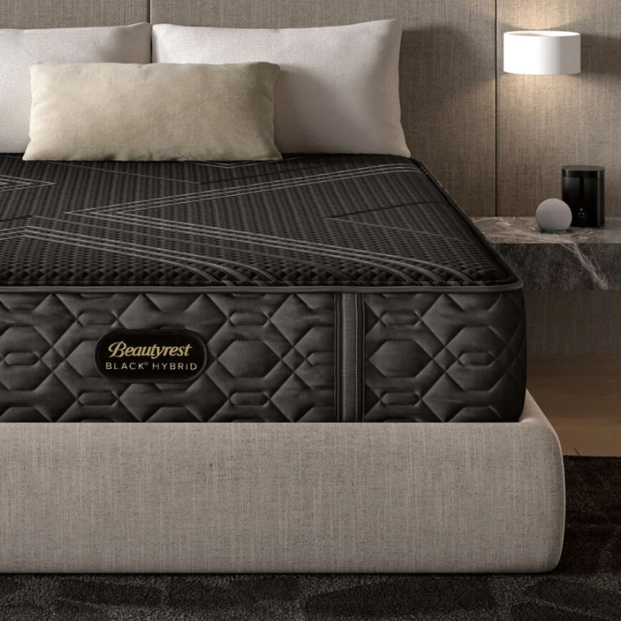 Luxury Beautyrest Black Hybrid mattress placed on a beige upholstered bed frame, with plush pillows and a modern nightstand in the background, creating a cozy and elegant bedroom setting.