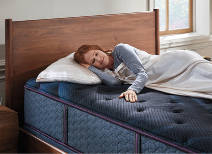 Woman laying on her right side with her head on a pillow as she rubs the top of a Beautyrest World Class mattress. 