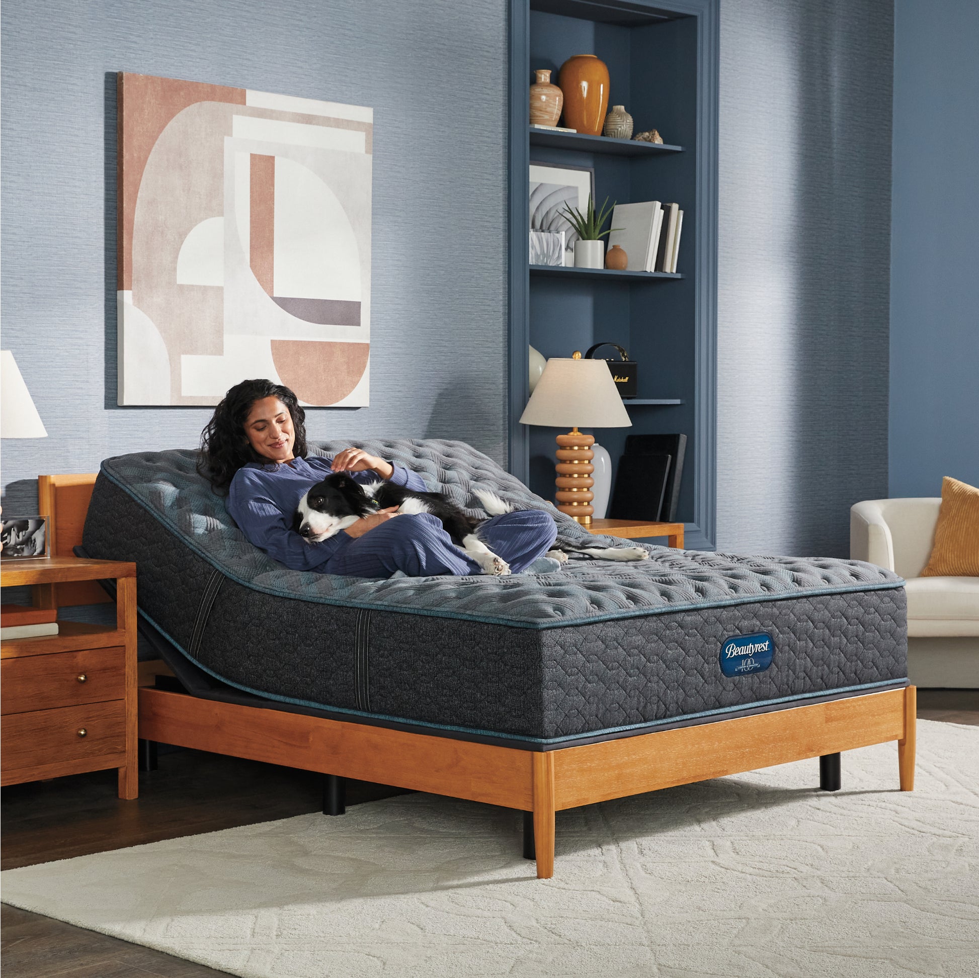 Woman sitting on a slightly elevated  on an adjustable base Beautyrest Innerspring Mattress sitting in a brown bed frame holding her dog