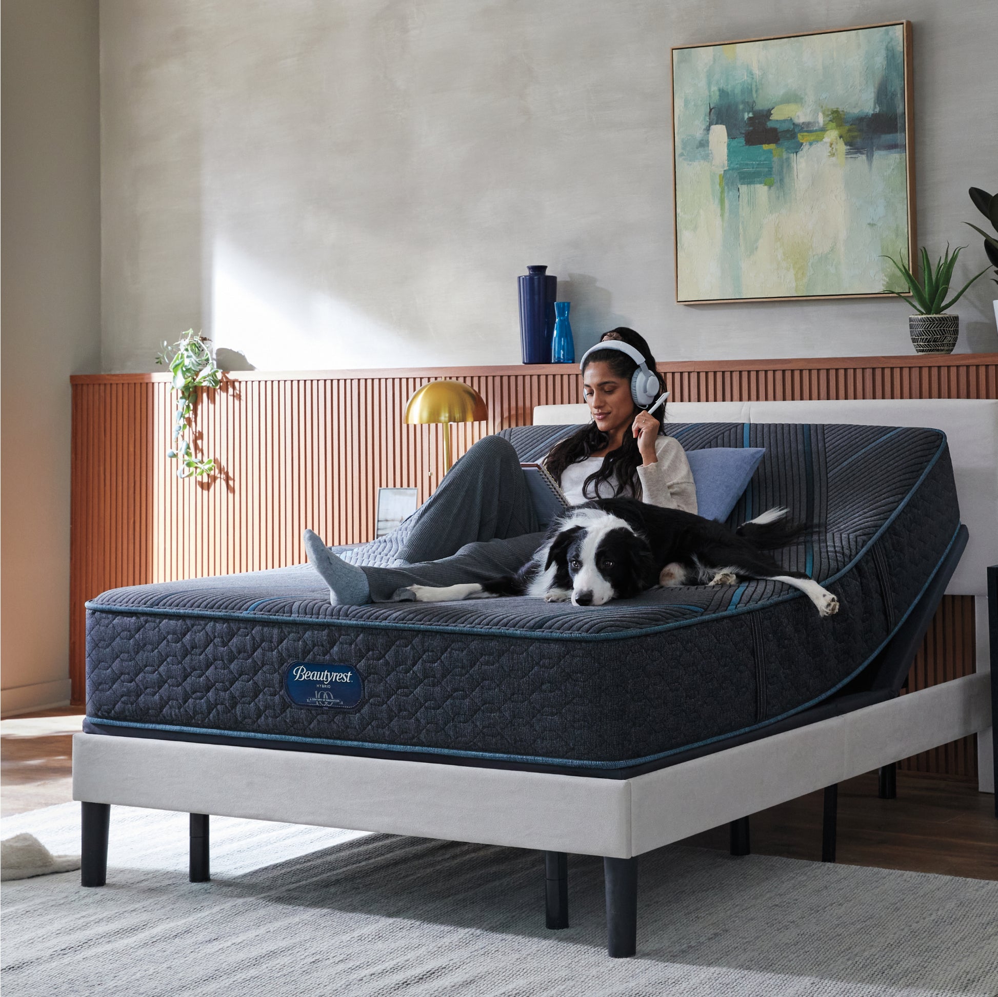 Woman sitting on Beautyrest Hybrid Mattress with her dog writing on a notepad with her mattress elevated on an adjustable base.