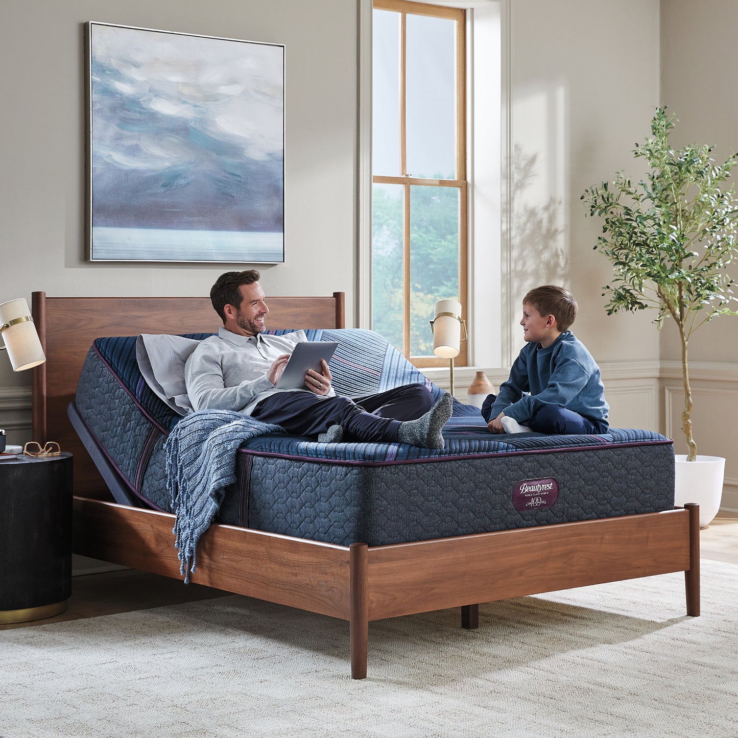 Man and his son sitting on a Beautyrest World Class mattress slightly elevated on an adjustable base sitting in a brown bed frame