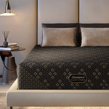 Beautyrest Black Hybid XCS firm mattress on a bed with decorative pillows in a modern bedroom setting.