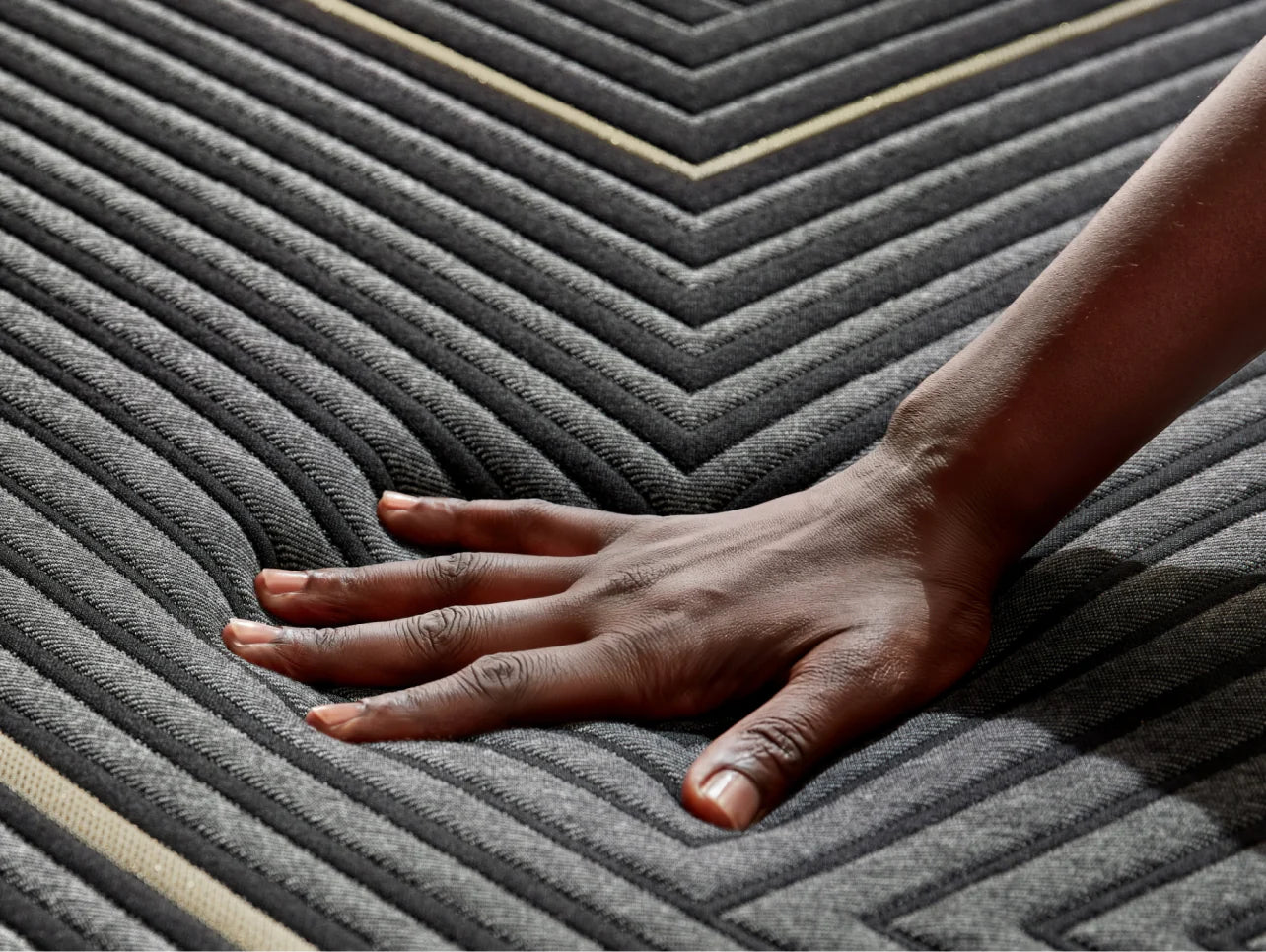 Close up of woman's hand pressing down on a smooth top hybrid mattress