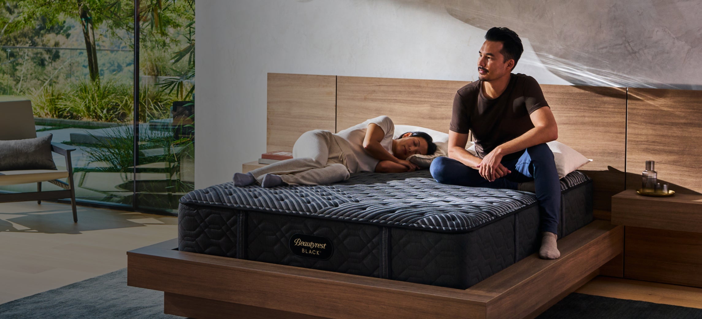 Man sitting on Beautyrest Black mattress while his wife sleeps.